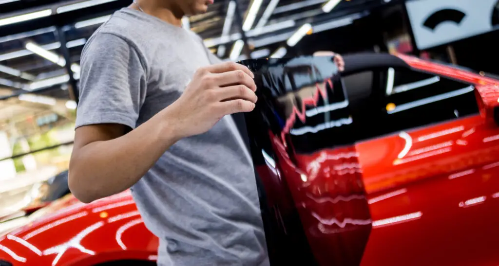 Applying tinting foil on a car window in a auto service. Red car at background