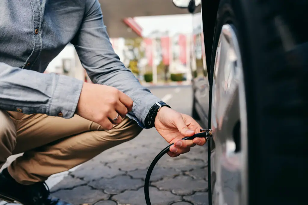 Close up of man crouching on the gas station and inflating tire.