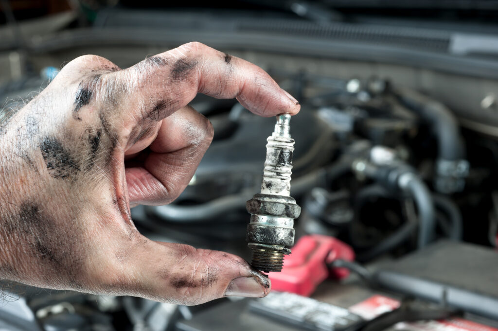 An auto mechanic holds an old, dirty sparkplug over a car engine he is tuning up.