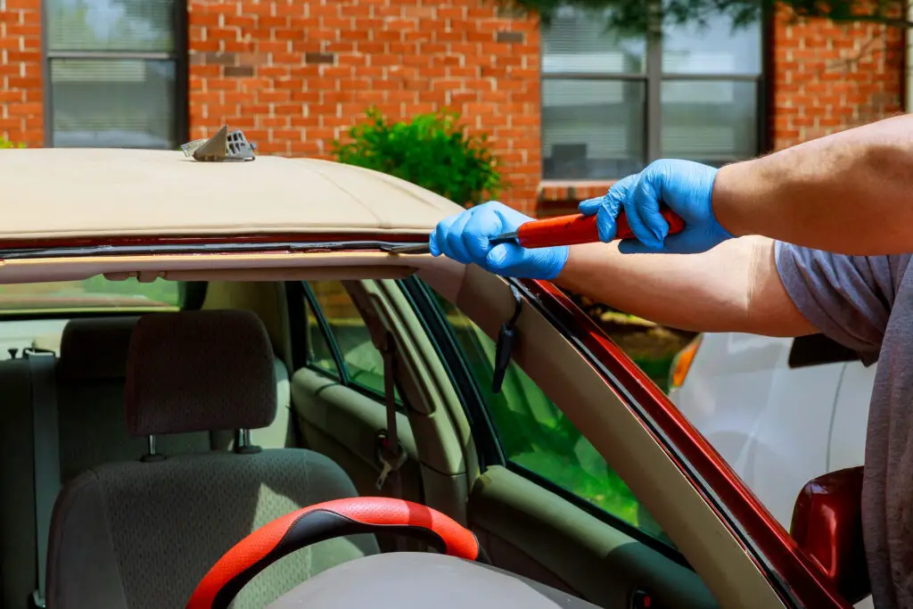 Technician removing old glue while replacing a windshield
