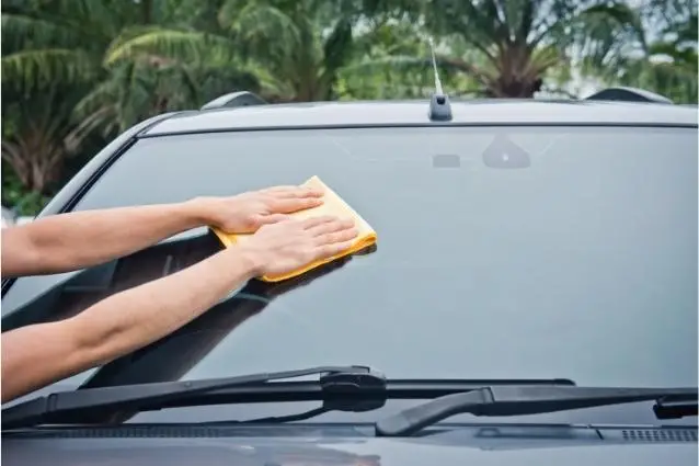 Person cleaning car's windshield with fiber cloth