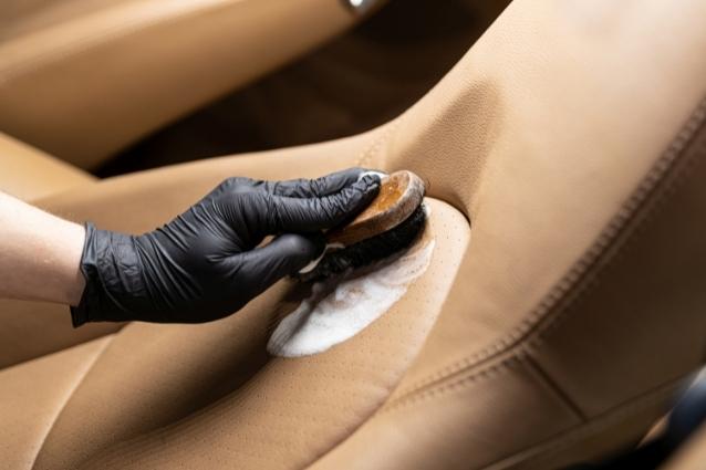 Person uses soft bristle brush to clean beige leather seat