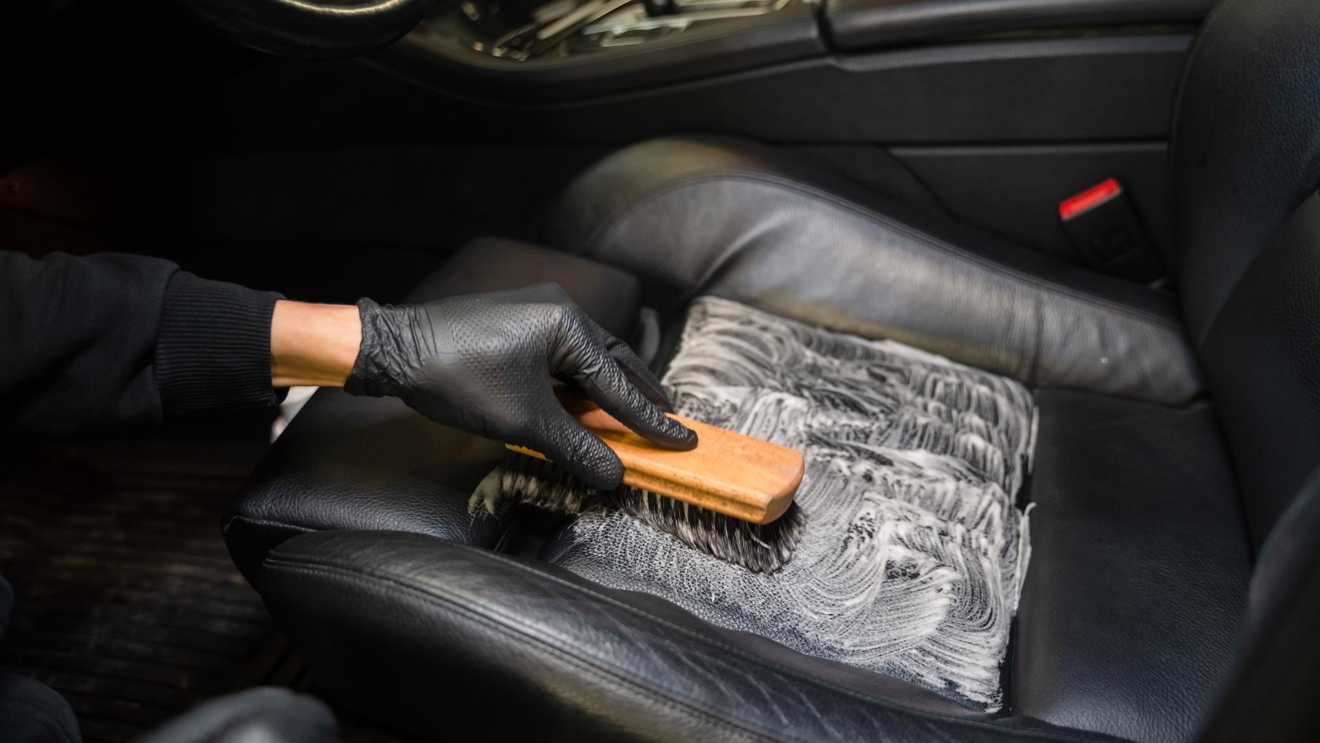 Hand in black nitrile gloves cleaning black leather driver seat with brush on a vehicle