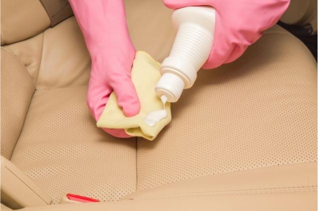 Person with pink rubber gloves applies leather seat conditioner on the special cloth before using it on beige car seat