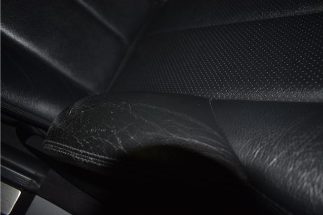 Slightly damaged black leather seat on a car, close up