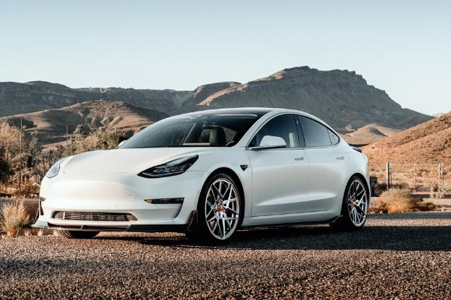 Nice white sporty Tesla Model 3, with custom bumper and wheels. Desert on background.