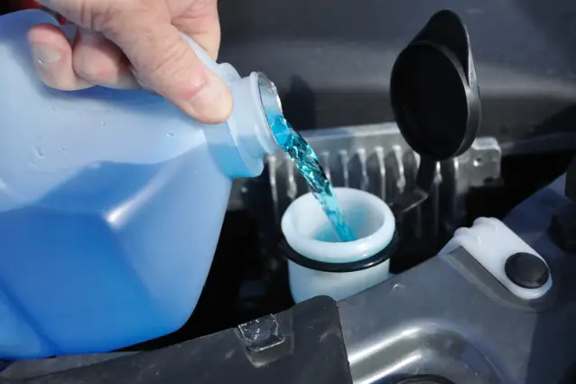 Person is filling up blue windshield washer fluid reservoir on a car, close up