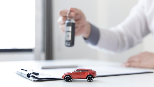 Agent holding car keys, registration form and little toy car on the table.