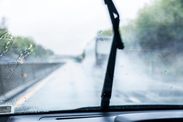 Windshield wiper blade in action, car is driving on the highway in the rain