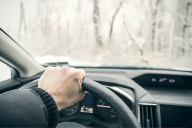 Person is driving a car in the winter, hand is on the steering wheel