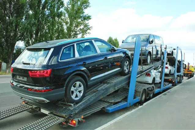 Truck loaded with brand new cars is parked on the street.