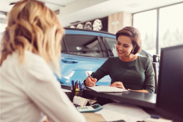 Woman is buying a car from the dealership, agent is preparing purchase contract for the customer.